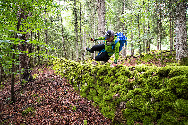 Thomas überquert eine moosige Mauer im Wald oberhalb von Le Brassus.